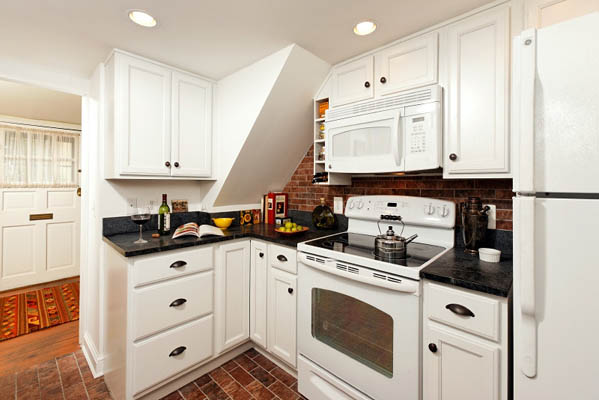 small, renovated kitchen with white cabinets, black countertops, and a brick flooring