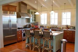 Kitchen interior with wicker bar-height chairs at a central island and three bright windows