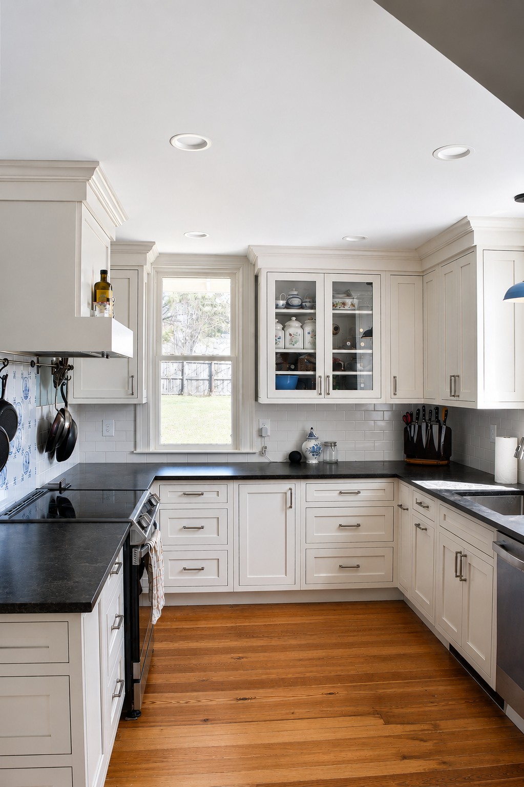 renovated kitchen with restored pine floors white inset cabinets, soap stone countertop, subway tile backsplash with accent tile over the stove and pot rail