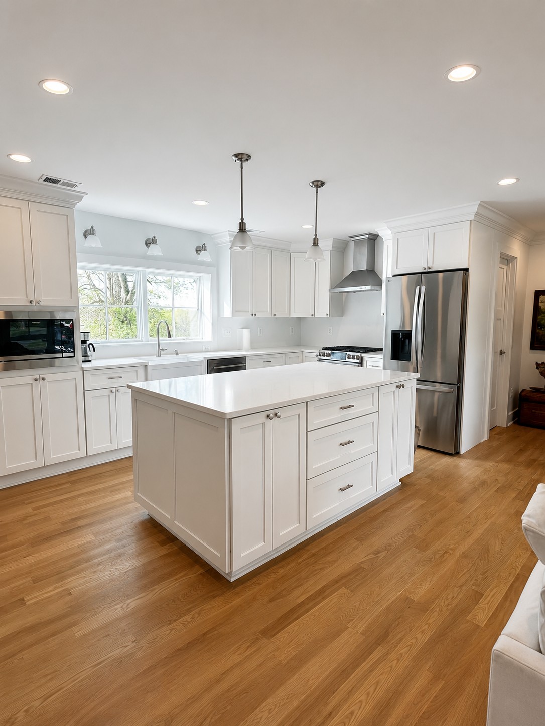 renovated kitchen white full overlay cabinets with crown molding to the ceiling and stainless steel appliances with neutral oak floors